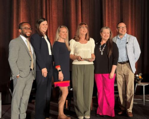 Amy Sapp holds the Patient Care Award trophy from NAPT while standing on stage with her colleagues from the UF Health Proton Therapy Institute.