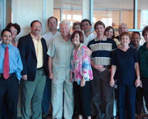 Group of men and women standing in a room with a glass wall in the background