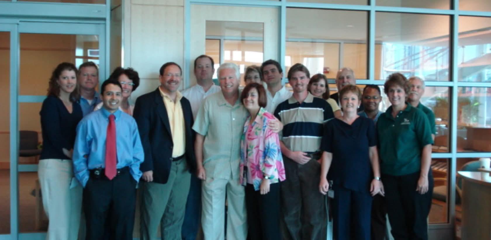Group of men and women standing in a room with a glass wall in the background