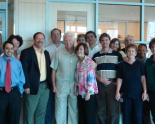 Group of men and women standing in a room with a glass wall in the background